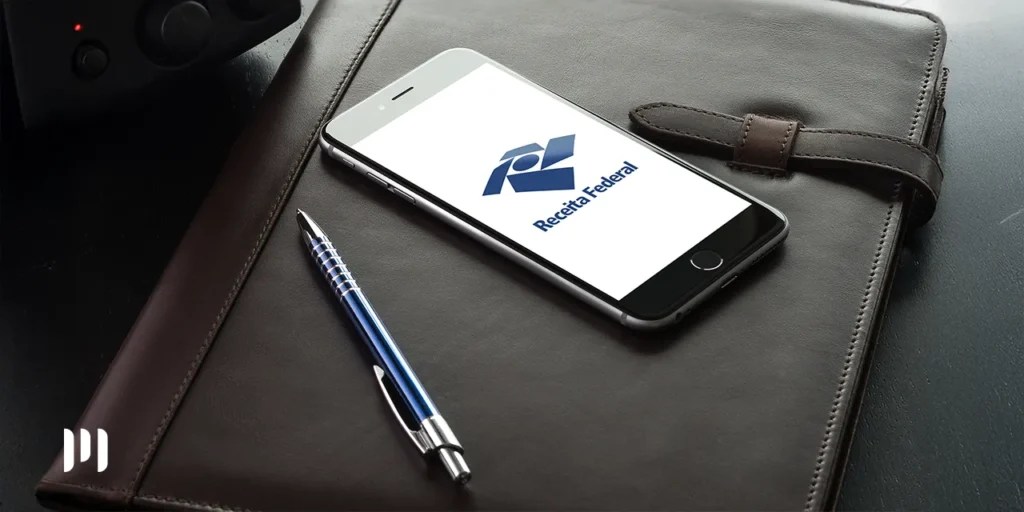 Um celular em cima de uma pasta de coruro na tela do celular a logo da Receita Federal simbolizando o Impoosto de Renda 2025