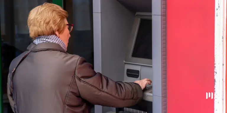 Uma senhora em frente ao caixa eletrônico de um banco. A imagem ilustra a notícia sobre o décimo terceiro dos aposentados.