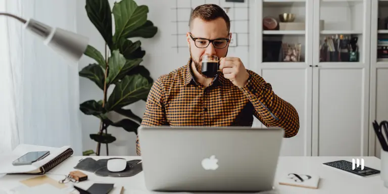 Homem tomando café enquanto lê no notebook sobre dedução de devoluções no lucro presumido.