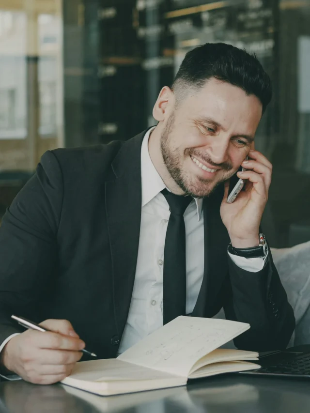 Homem de terno falando ao telefone enquanto escreve.